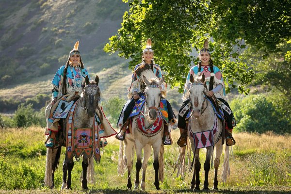three women, dressed in traditional native american outfits, sit atop paint horses in the North Central Idaho region